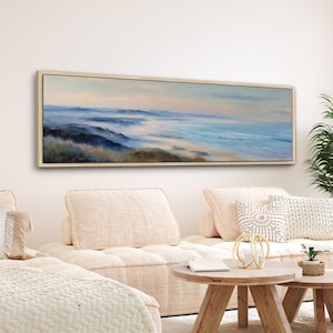 Puede incluir: Una pintura de paisaje rectangular y alargada con marco de madera clara. La obra representa una escena costera brumosa con agua azul, colinas onduladas y una paleta de colores pastel suaves.