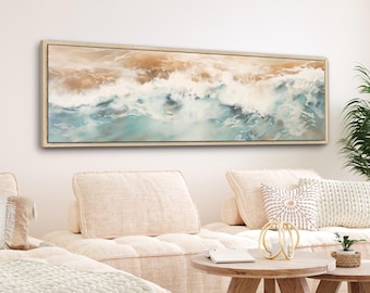 Puede incluir: Una pintura larga y horizontal de olas del océano rompiendo en una playa de arena. La pintura está enmarcada en un marco de madera clara y está colgada en una pared blanca sobre un sofá beige.