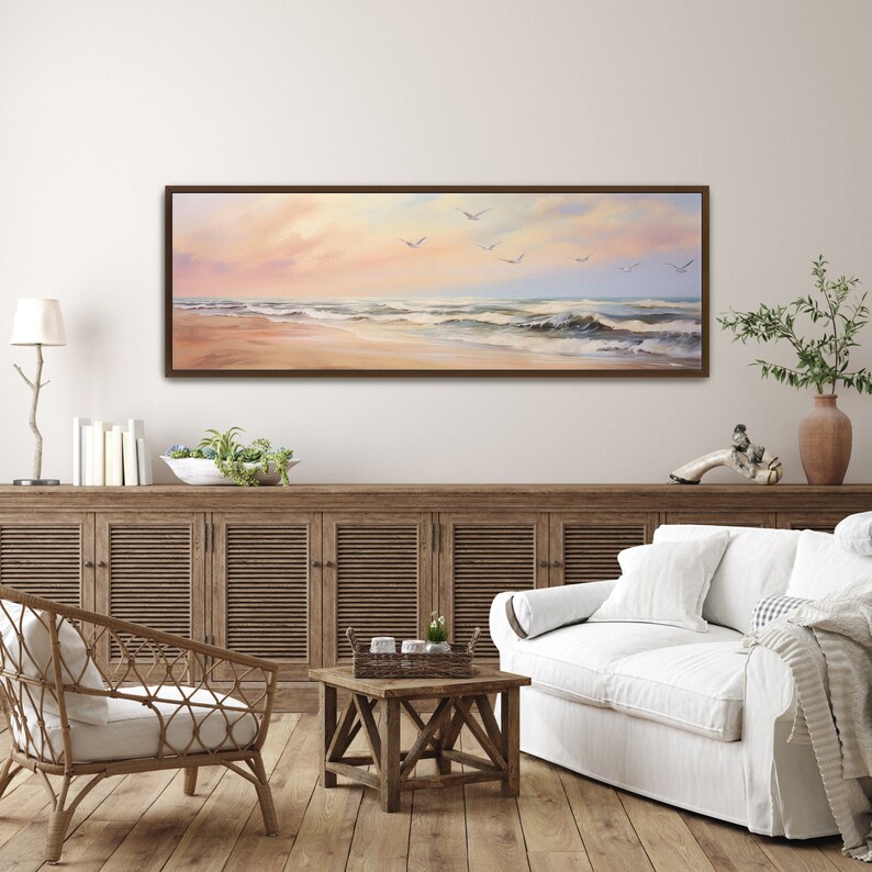 May include: A framed painting of a seascape with a sandy beach and waves crashing on the shore. The sky is a soft pink and orange, and there are white birds flying overhead.