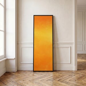 May include: A tall, rectangular wall art piece featuring a vibrant gradient of orange and yellow hues. The artwork is enclosed within a thin, black frame, creating a sharp contrast against the bright, warm colors of the central canvas panel.