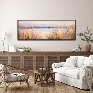 Puede incluir: Una pintura larga y horizontal de una escena de lago con una paleta de colores suave y tenue. La pintura presenta un lago con una costa distante, hierbas altas y un cielo brumoso. Los colores son principalmente tonos de rosa, morado y azul.