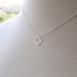 Könnte beinhalten: Eine silberne Kettenkette mit einem kleinen, diamantförmigen Anhänger.