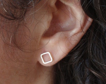 May include: A pair of silver square stud earrings. The earrings are simple and minimalist, with a thin wire frame.