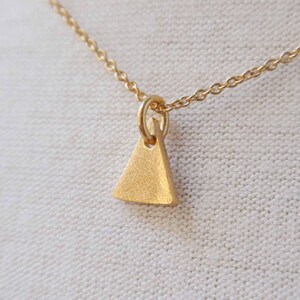 Puede incluir: Un collar de cadena de oro con un pequeño colgante triangular.