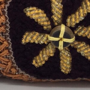 Puede incluir: Primer plano de una tela marr&oacute;n con un dise&ntilde;o de flor de cuentas amarillas. La flor tiene un centro marr&oacute;n oscuro con una cruz de cuentas amarillas.
