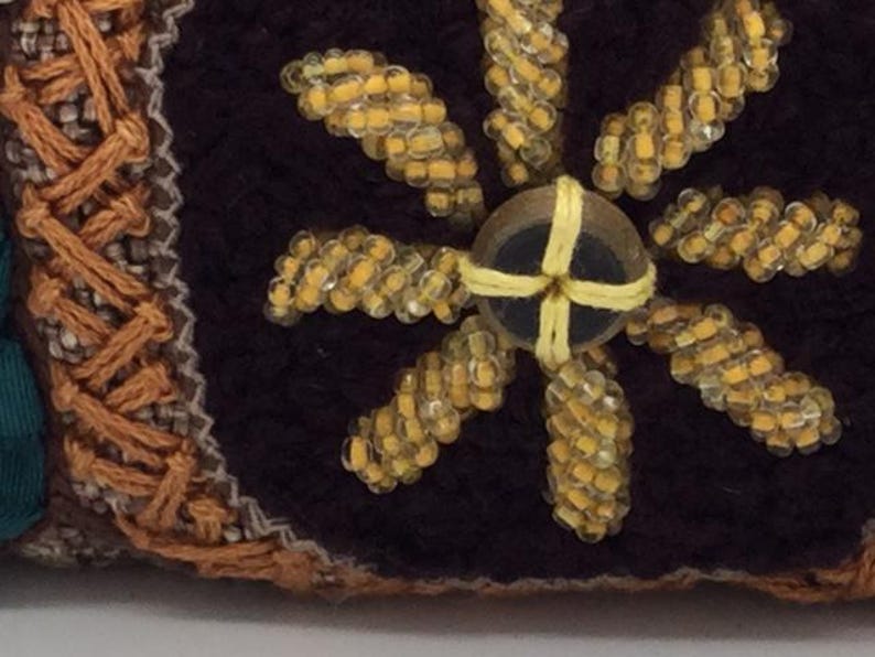 Puede incluir: Primer plano de una tela marr&oacute;n con un dise&ntilde;o de flor de cuentas amarillas. La flor tiene un centro marr&oacute;n oscuro con una cruz de cuentas amarillas.