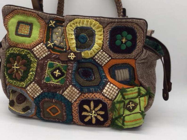 Puede incluir: Un bolso tote de patchwork marr&oacute;n con una variedad de cuadrados de ganchillo de colores. Los cuadrados son en tonos de verde, azul, amarillo, naranja y marr&oacute;n. El bolso tiene cierre de cremallera y asa superior.