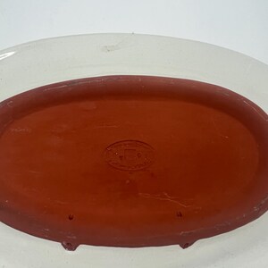 May include: A white oval ceramic serving dish with a red terracotta insert. The insert has a small round stamp with the text "MADE IN ITALY".