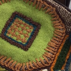Puede incluir: Primer plano de una tela verde con bordados marrones y naranjas. La tela tiene un patr&oacute;n cuadrado en el centro con un borde marr&oacute;n y un borde azul y marr&oacute;n alrededor del cuadrado.
