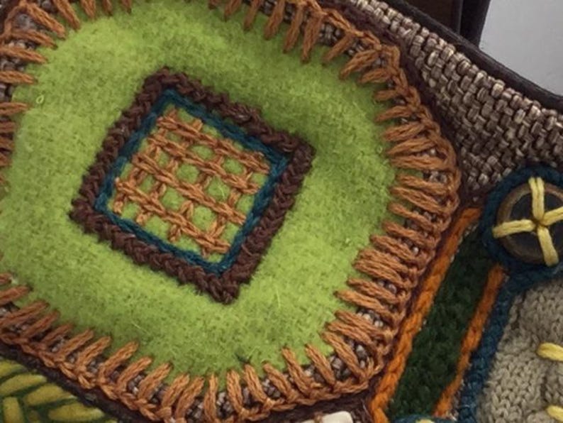 Puede incluir: Primer plano de una tela verde con bordados marrones y naranjas. La tela tiene un patr&oacute;n cuadrado en el centro con un borde marr&oacute;n y un borde azul y marr&oacute;n alrededor del cuadrado.