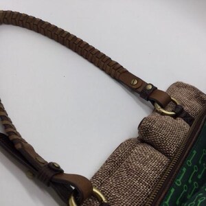 Puede incluir: Un bolso de hombro de cuero marr&oacute;n con una correa trenzada. El bolso tiene un cuerpo de tela verde con un patr&oacute;n de llaves. El bolso tiene una solapa de tela marr&oacute;n con cierre de cremallera.