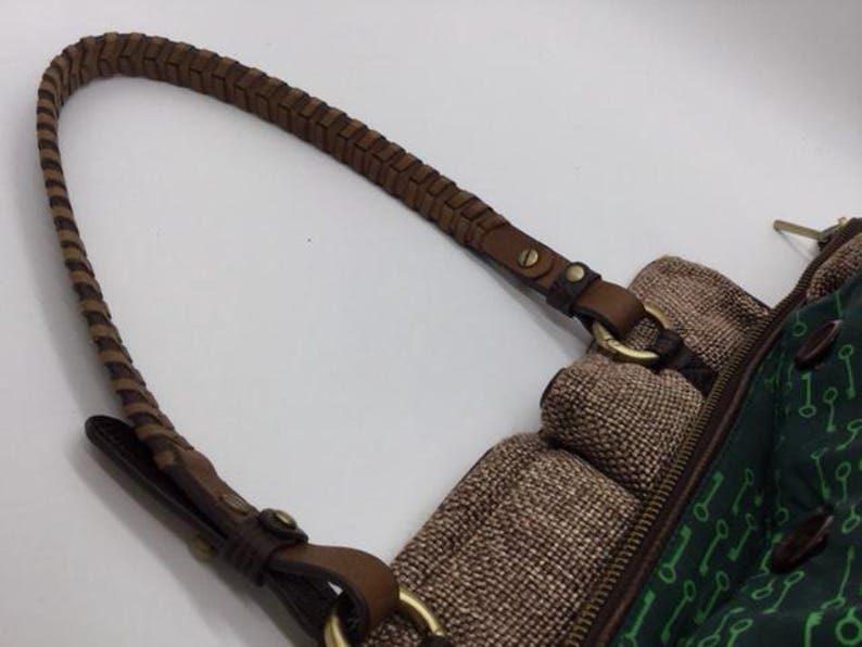 Puede incluir: Un bolso de hombro de cuero marr&oacute;n con una correa trenzada. El bolso tiene un cuerpo de tela verde con un patr&oacute;n de llaves. El bolso tiene una solapa de tela marr&oacute;n con cierre de cremallera.