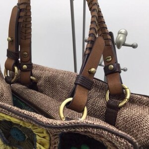 Puede incluir: Un bolso tote tejido marr&oacute;n con correas de cuero y herrajes dorados. El bolso tiene un dise&ntilde;o de patchwork colorido en la parte inferior.