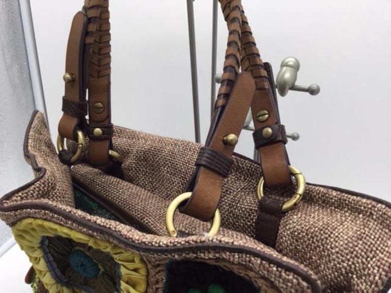 Puede incluir: Un bolso tote tejido marr&oacute;n con correas de cuero y herrajes dorados. El bolso tiene un dise&ntilde;o de patchwork colorido en la parte inferior.
