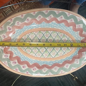 May include: A large oval serving dish with a pink, green, and blue floral pattern. The dish is made of ceramic and has a glazed finish.