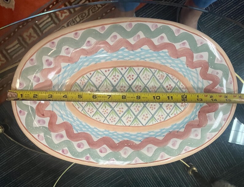 May include: A large oval serving dish with a pink, green, and blue floral pattern. The dish is made of ceramic and has a glazed finish.