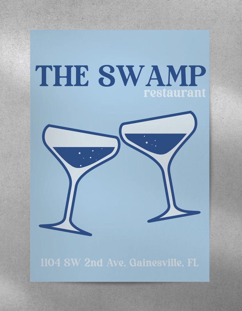 May include: A blue and white poster with the text "THE SWAMP restaurant" and two blue martini glasses clinking together. The address "1104 SW 2nd Ave, Gainesville, FL" is printed at the bottom.