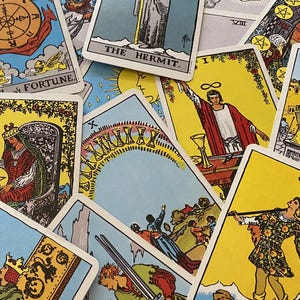 May include: A collection of tarot cards with various illustrations and titles. The cards feature vibrant colors, including yellow, blue, and red. Some cards display figures, symbols, and text such as "The Hermit" and "Fortune".