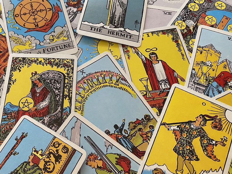 May include: A collection of tarot cards with various illustrations and titles. The cards feature vibrant colors, including yellow, blue, and red. Some cards display figures, symbols, and text such as "The Hermit" and "Fortune".