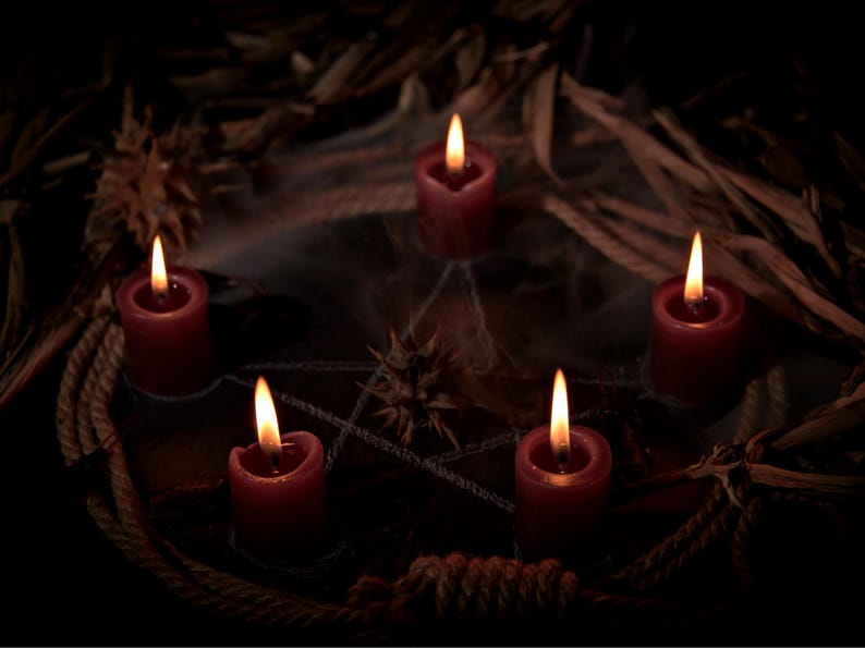 May include: Five red candles with lit flames arranged in a circle, surrounded by a rustic arrangement of rope, dried leaves, and a spiderweb. The candles are the focal point, casting a warm glow against the dark background, creating a mystical ambiance.