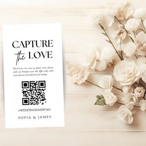 May include: White card with black text that reads "CAPTURE the LOVE" and a QR code. The text below the QR code reads "#WEDDINGHASHTAG SOFIA & JAMES".
