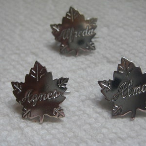 May include: Three silver maple leaf place card holders with the names "Alfreda", "James", and "Alma" engraved on them.