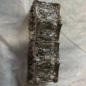 Pu&ograve; includere: Un braccialetto d'argento con un designo a filigrana. Il braccialetto &egrave; composto da quattro sezioni, ognuna con un motivo diverso. Il braccialetto &egrave; largo circa 5 cm.