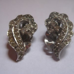 May include: A pair of silver tone clip-on earrings with a leaf design and clear rhinestones.