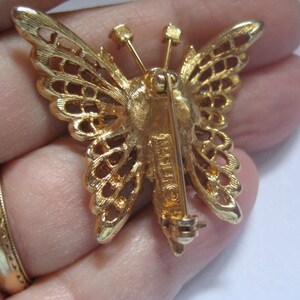 May include: Gold-tone butterfly brooch with a filigree design and a pin back. The brooch is marked "Made in France".