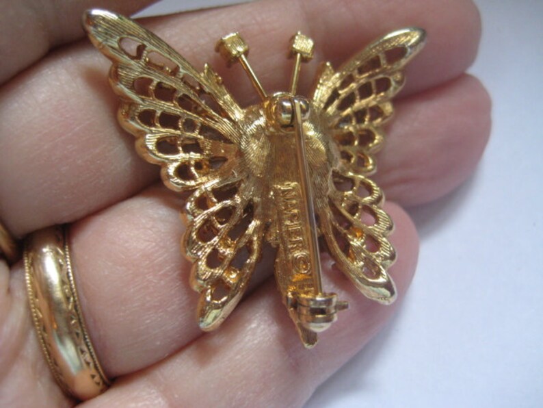May include: Gold-tone butterfly brooch with a filigree design and a pin back. The brooch is marked "Made in France".