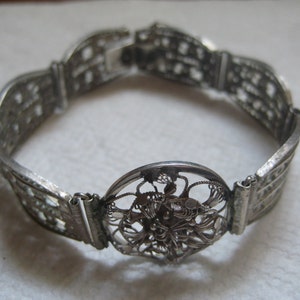May include: A silver filigree bracelet with a circular design in the center. The bracelet is made of delicate, intricate metalwork.