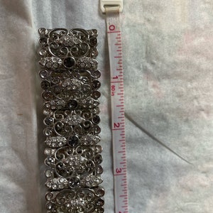 Pu&ograve; includere: Un braccialetto d'argento con un design a filigrana e strass trasparenti e grigio scuro. Il braccialetto &egrave; lungo 5 cm.