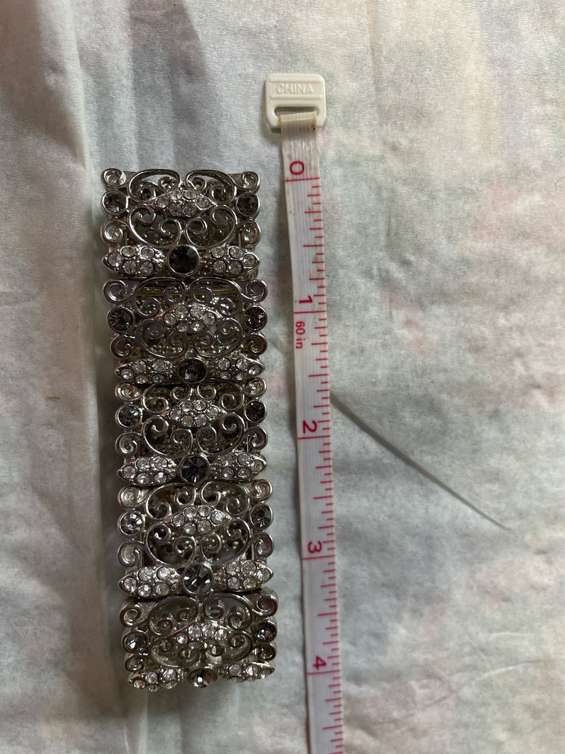 Pu&ograve; includere: Un braccialetto d'argento con un design a filigrana e strass trasparenti e grigio scuro. Il braccialetto &egrave; lungo 5 cm.