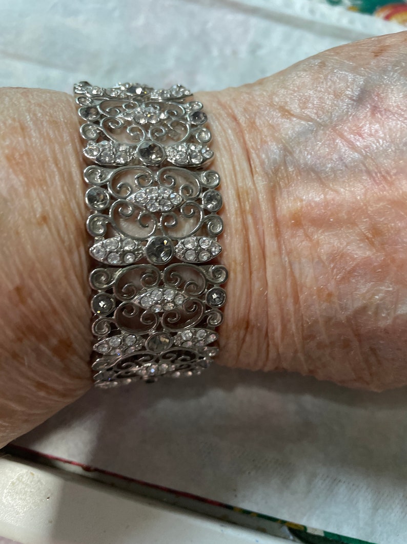 Pu&ograve; includere: Un braccialetto d'argento con un delicato design a filigrana e strass trasparenti.