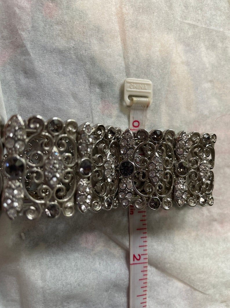 Pu&ograve; includere: Un braccialetto d'argento con un design a filigrana e strass trasparenti e neri. Il braccialetto ha un diametro di circa 5 cm.