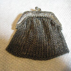 May include: A silver chainmail purse with a decorative clasp. The purse is closed and has a slightly rounded shape.