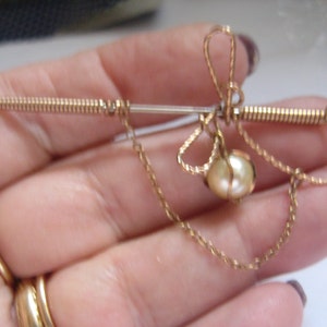 May include: A gold-toned brooch with a pearl pendant and a coiled wire design. The brooch is shaped like a bow with a chain attached to the bottom.