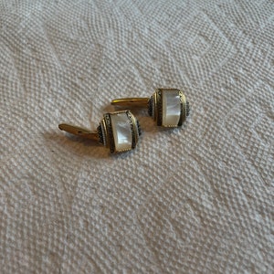 May include: A pair of gold cufflinks with white mother of pearl insets. The cufflinks have a decorative design around the edges.