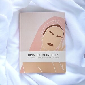 Peut inclure: Une couverture de journal illustrée rose et marron avec le visage d'une femme et le texte "Brin de Bonheur" et "Mon Journal d'Epanouissement Quotidien".