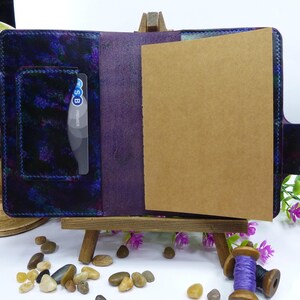 May include: A purple leather notebook cover featuring a mottled blue and black pattern on the left panel, a card slot containing a TSB Premier card, and a plain brown paper insert on the right side, all held together by visible dark stitching.