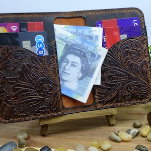 May include: Open brown leather wallet with a floral embossed pattern. The wallet contains credit cards and British five-pound notes. The wallet is displayed open, revealing its internal compartments and contents.