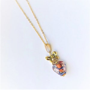 May include: A gold chain necklace with a heart-shaped pendant. The pendant is made of clear glass with orange and blue flecks and a gold bow on top.