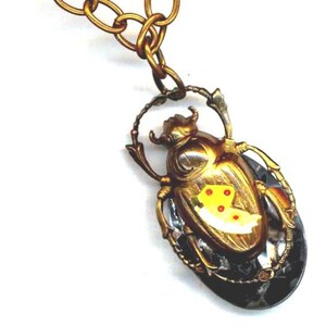 May include: A gold-tone beetle pendant necklace with a clear crystal body and yellow and red accents. The beetle is suspended from a gold-tone chain.
