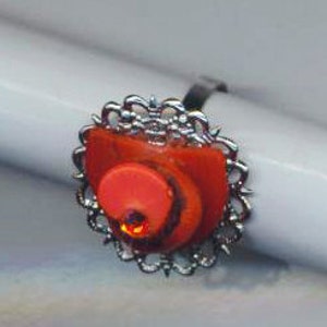 Puede incluir: Un anillo de plata con un dise&ntilde;o de espiral rojo y naranja engastado en un marco de filigrana de plata.