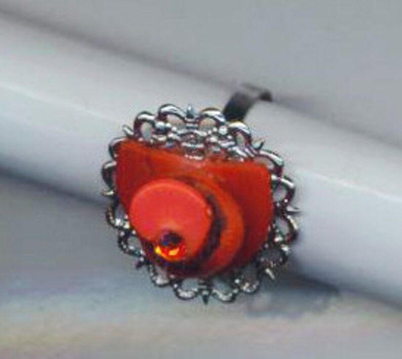 Puede incluir: Un anillo de plata con un dise&ntilde;o de espiral rojo y naranja engastado en un marco de filigrana de plata.