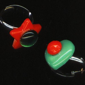 May include: Two rings with colorful glass stones. One ring has a red star-shaped stone with a green center. The other ring has a green heart-shaped stone with a red center.