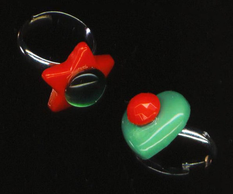 May include: Two rings with colorful glass stones. One ring has a red star-shaped stone with a green center. The other ring has a green heart-shaped stone with a red center.