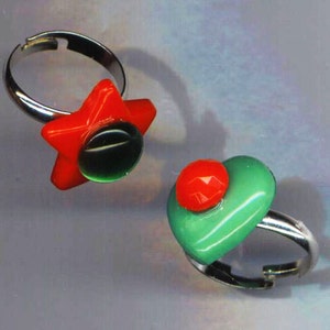 May include: Two silver rings with colorful glass accents. One ring features a red star with a green center. The other ring has a green heart with a red center.