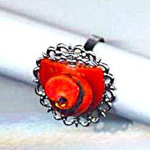 Puede incluir: Un anillo de concha roja y negra con un dise&ntilde;o de filigrana plateada.