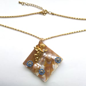 May include: A gold chain necklace with a pendant featuring a shell with a gold cherub and blue rhinestones.